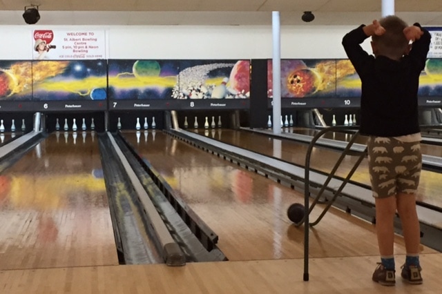 Preschooler raises his hands after rolling a bowling ball down 