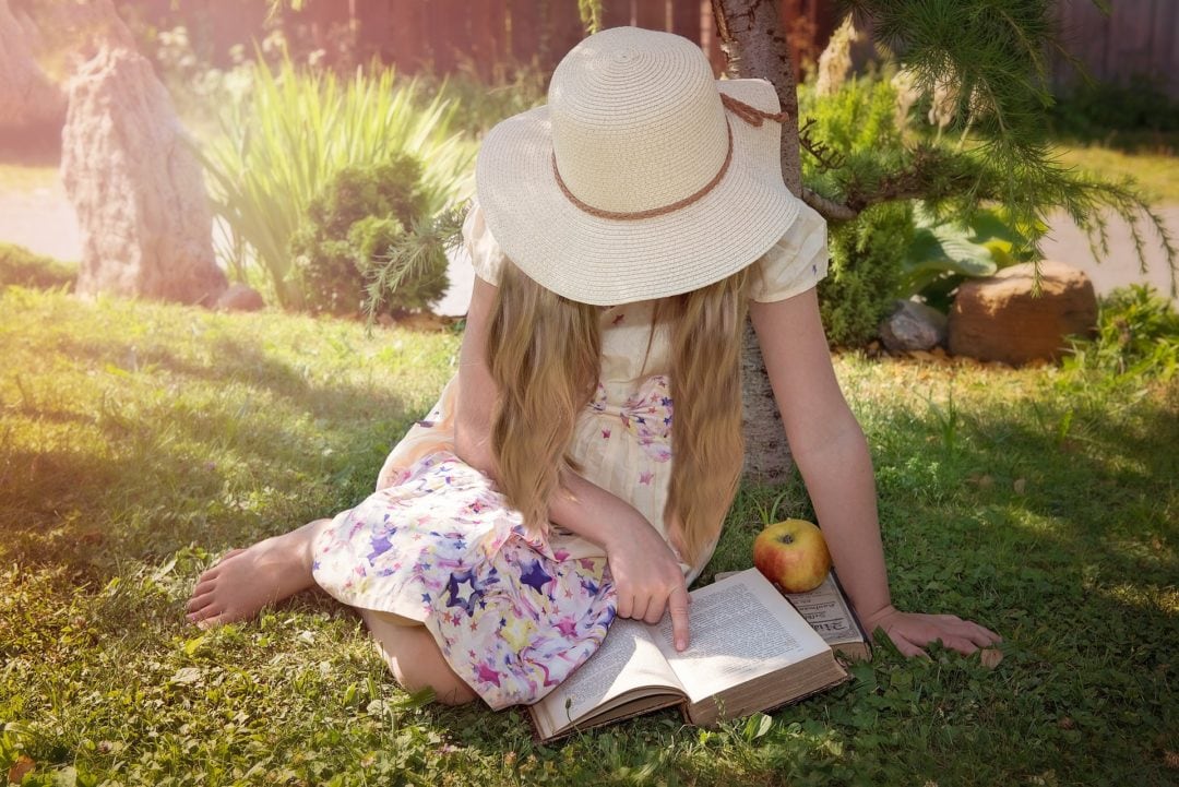 Little girl sitting on grass reading a book during golden hour light