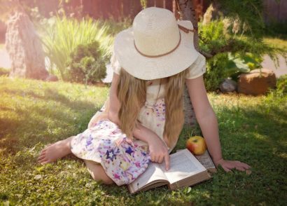 Little girl sitting on grass reading a book during golden hour light