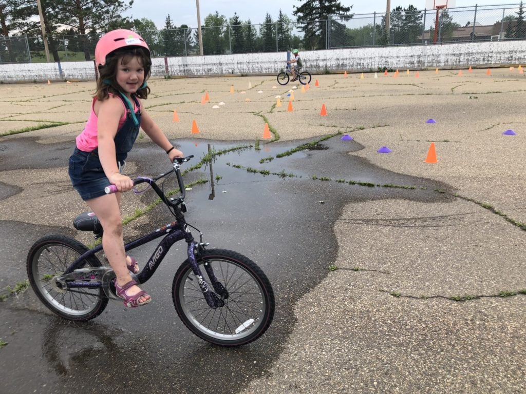 Young girl rides standing on her bike around a pylon obstacle course.
