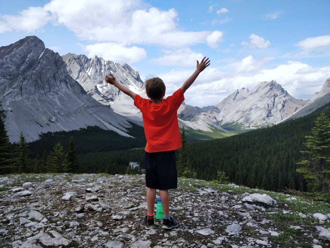 Kid raising arms in victory with mountains in the background