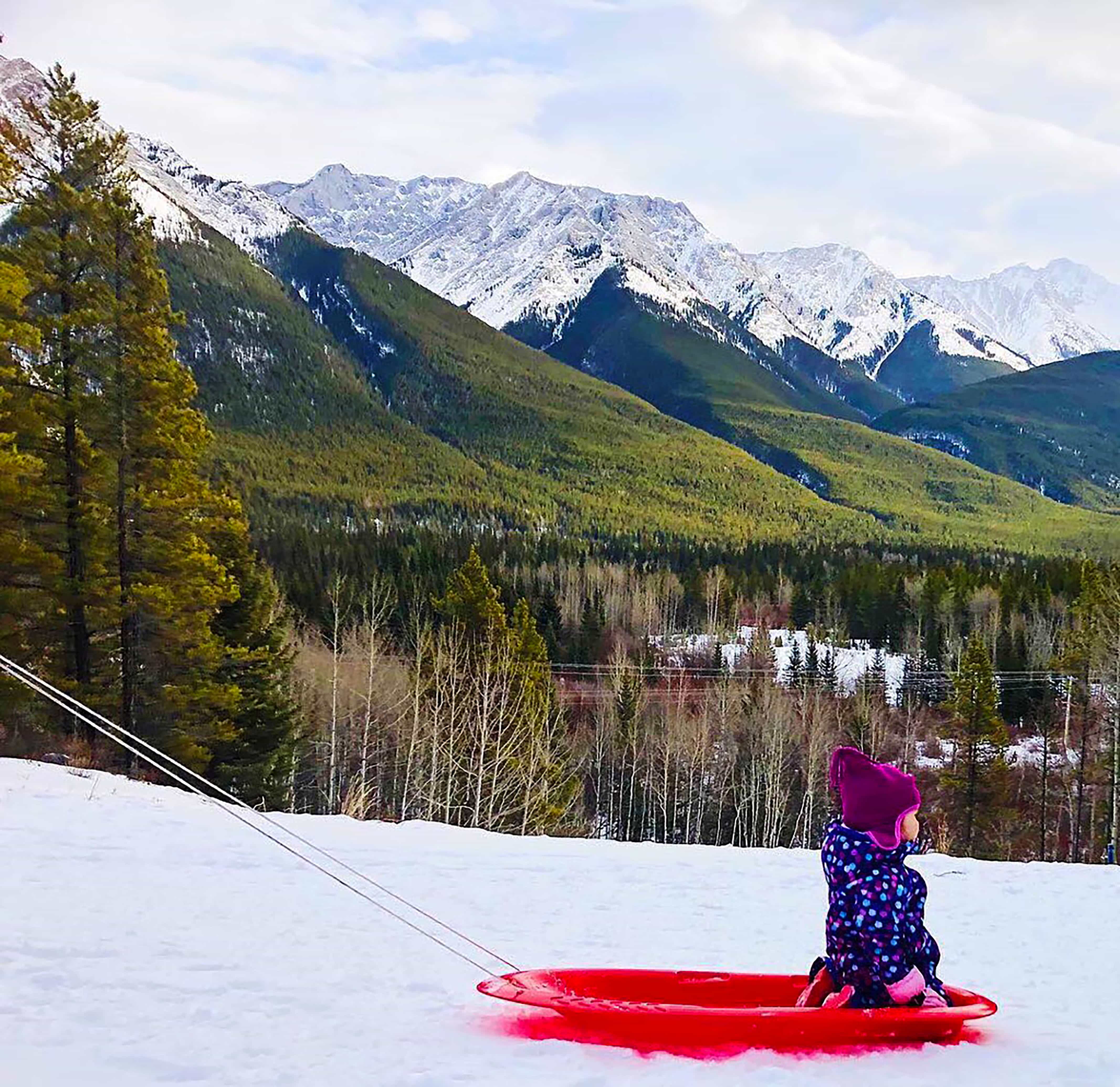 Child being pulled on red sled with mountains in the background