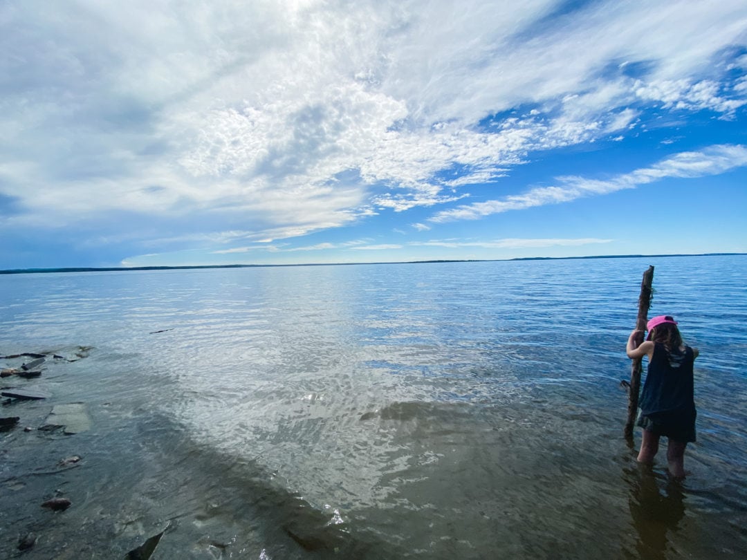 Child standing on the shore of Chip Lake with a large piece of driftwood as a walking stick.