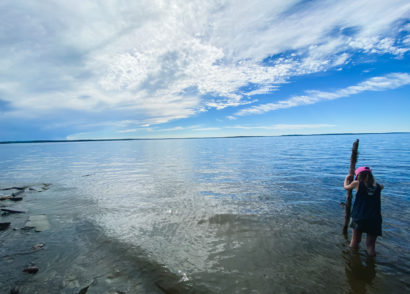 Child standing on the shore of Chip Lake with a large piece of driftwood as a walking stick.