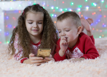 Kids in Christmas clothes looking at a cell phone
