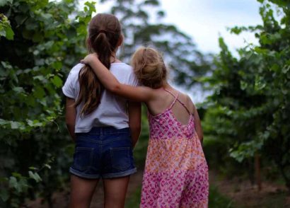Girls in summer clothing looking away from the camera, surrounded by bushes