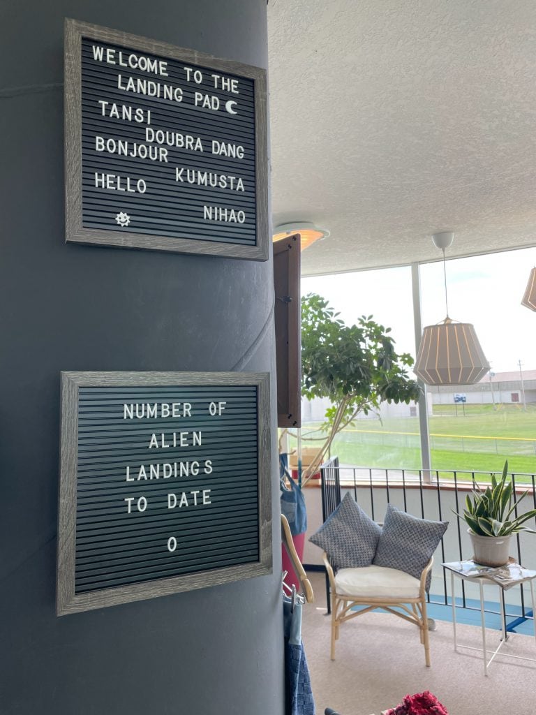 Interior of the St Paul UFO Landing Pad Visitor Centre with two signs. The first reads "Welcom to the Landing Pad. Tansi. Doubra Dang. Bonjour. Kumasta. Hello. Nihao." The second reads "Number of Alien Landings to Date: 0"