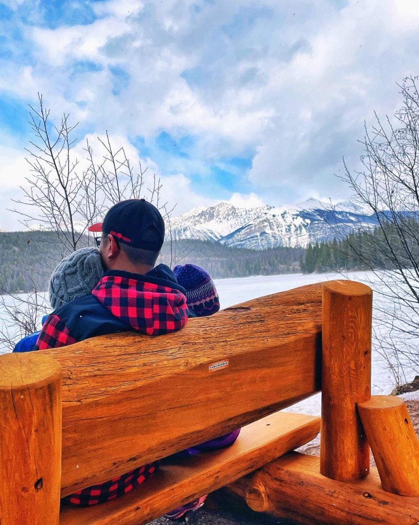 Dad and kids sitting on wood bench overlooking Pyramid Lake in Jasper National Park