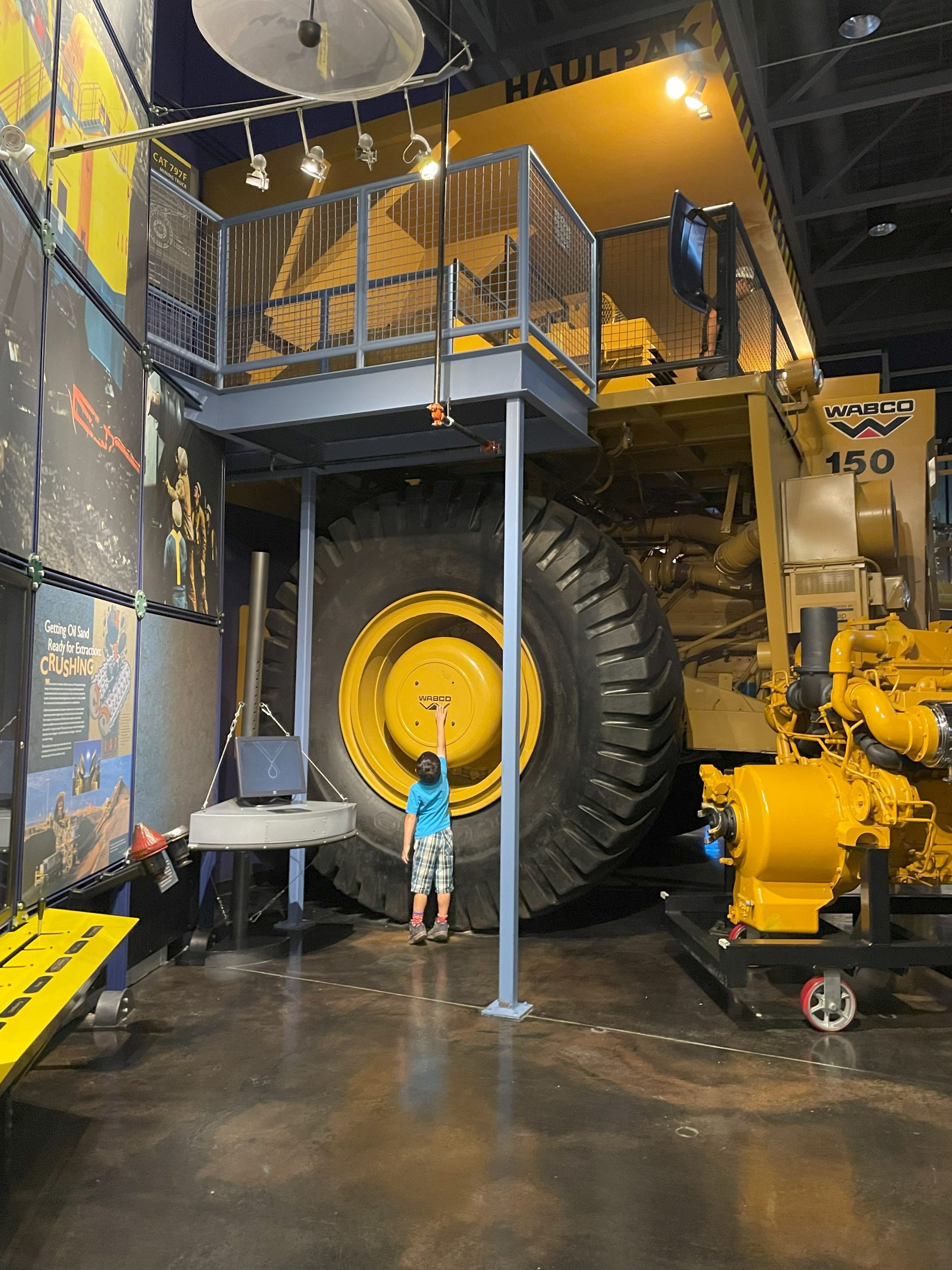 Little boy stretches to touch the hubcap of a WABCO 150 Heavy Hauler at Oil Sands Discovery Center in Fort McMurray