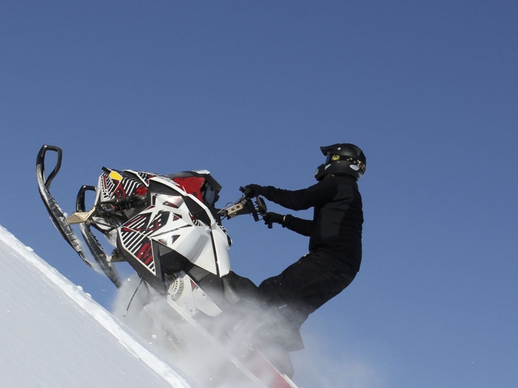 Person in black riding a white snowmobile. up a hill (source: Canva).