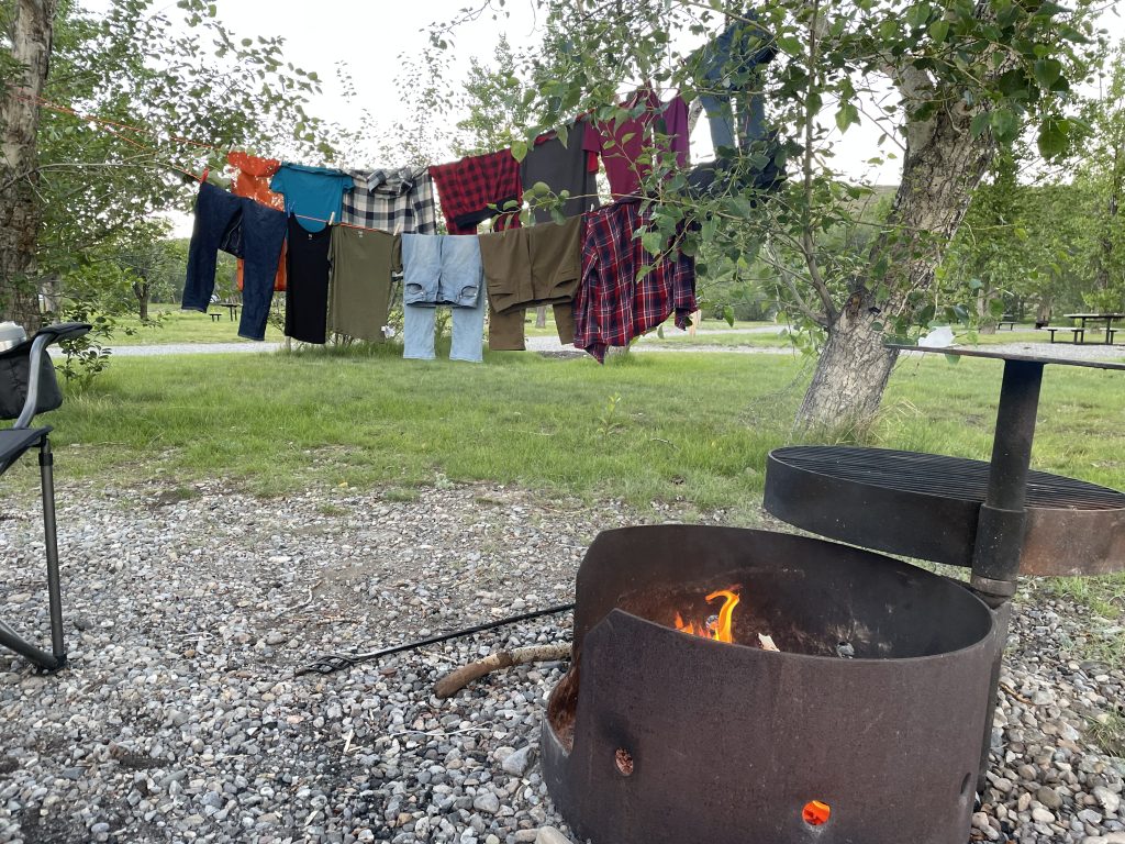 Two rows of laundry hanging on a line to dry between trees with a campfire in the foreground.